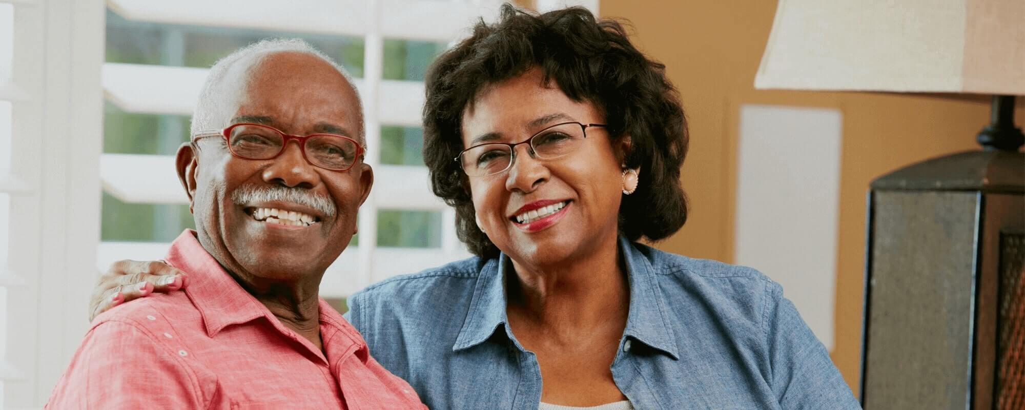 Older couple with dental implants smiling at the camera sat next to each other in our Staffordshire dental practice.